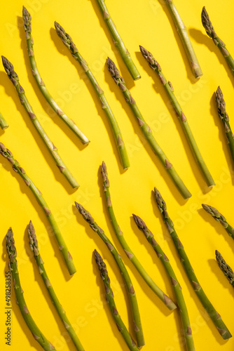 Overhead view of scattered raw green asparagus over yellow background