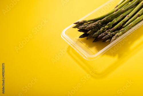 High angle view of raw asparagus in plastic container by copy space over yellow background