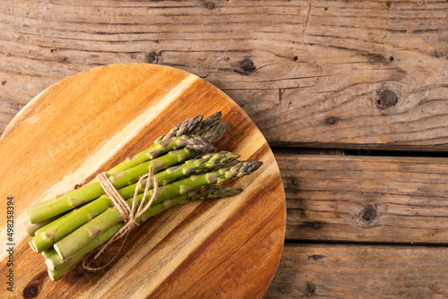 Directly above view of string tied raw asparagus vegetable bunch on wooden cutting board over table