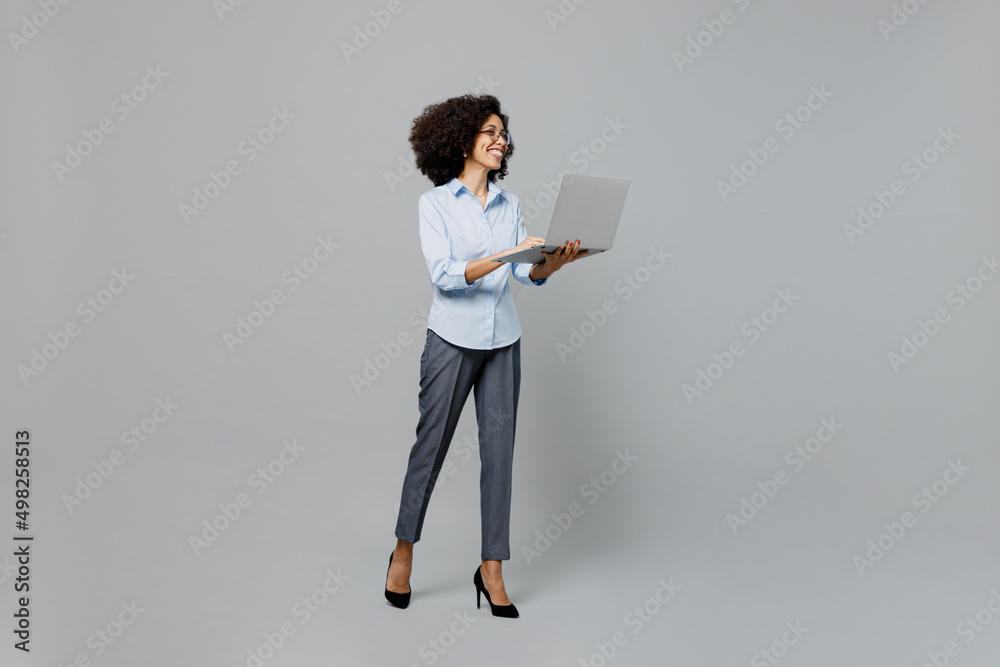 Full body fun successful young employee business corporate lawyer woman of African American ethnicity in classic formal shirt at office hold use work on laptop pc computer isolated on grey background.