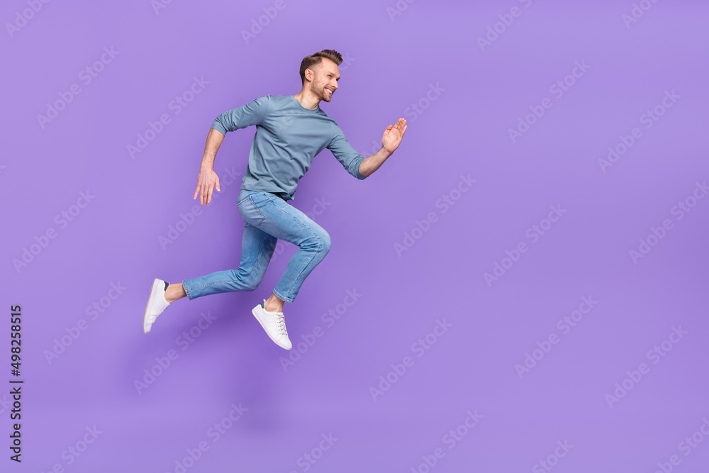 Photo of handsome charming guy dressed grey shirt jumping high running fast empty space isolated purple color background