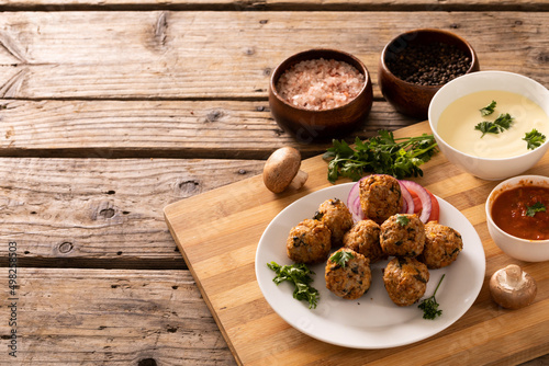 High angle view of fresh meatballs in plate with seasoning and dip bowls on wooden table