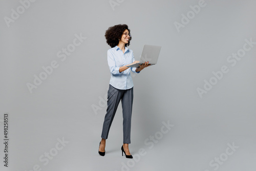 Full body fun successful young employee business corporate lawyer woman of African American ethnicity in classic formal shirt at office hold use work on laptop pc computer isolated on grey background.