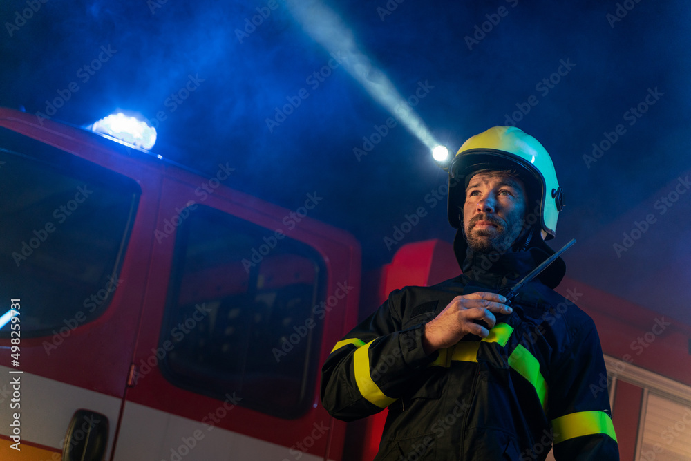 Obraz premium Low angle view of firefighter with fire truck in background at night.