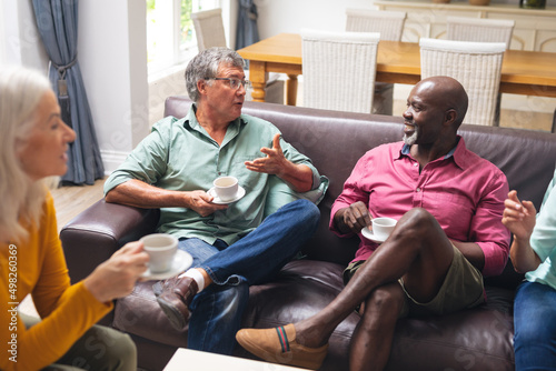 Multiracial senior male and female friends talking while having coffee together at home