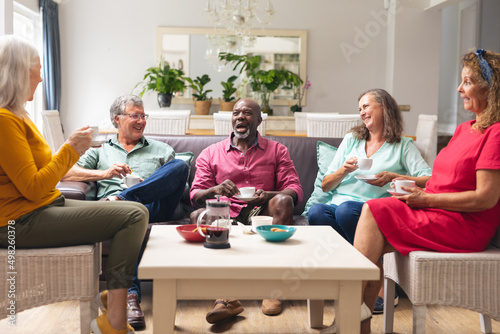 Happy multiracial senior female and male friends talking while having coffee together at home