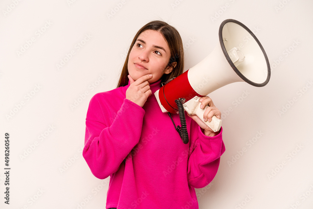 Young caucasian woman holding a megaphone isolated on white background looking sideways with doubtful and skeptical expression. Young caucasian woman holding a megaphone isolated on white background looking sideways with doubtful and skeptical expression.