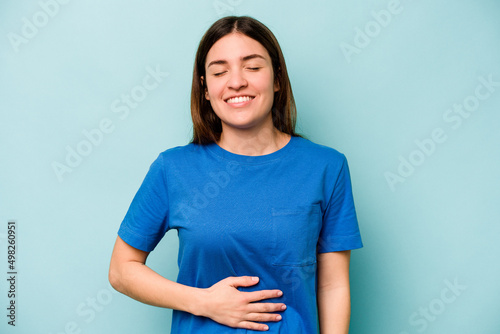 Young caucasian woman isolated on blue background touches tummy, smiles gently, eating and satisfaction concept.