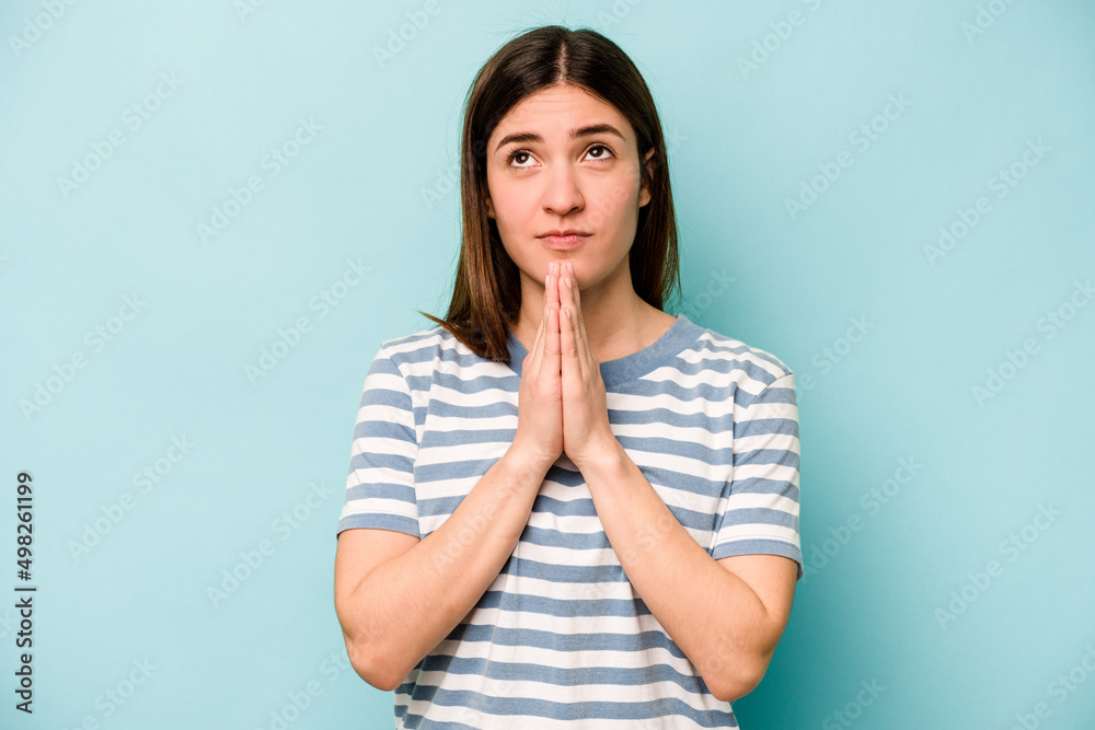 Young caucasian woman isolated on blue background holding hands in pray near mouth, feels confident. Young caucasian woman isolated on blue background holding hands in pray near mouth, feels confident.