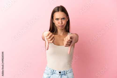 Young woman over isolated pink background showing thumb down with two hands