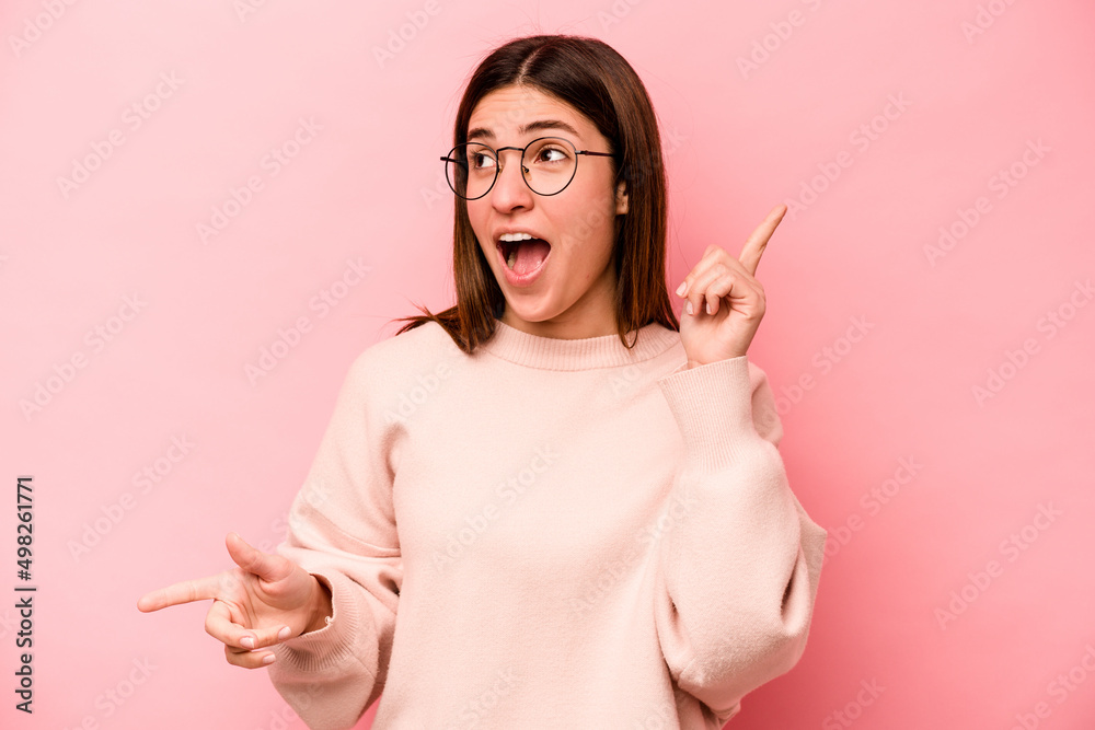 Obraz premium Young caucasian woman isolated on pink background pointing to different copy spaces, choosing one of them, showing with finger.