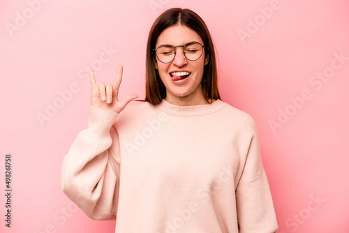 Young caucasian woman isolated on pink background showing rock gesture with fingers