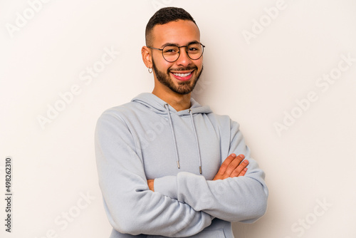 Young hispanic man isolated on white background who feels confident, crossing arms with determination.