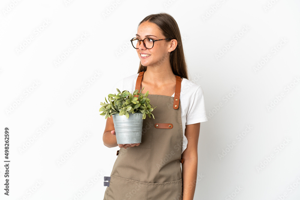 Gardener girl holding a plant over isolated white background looking side