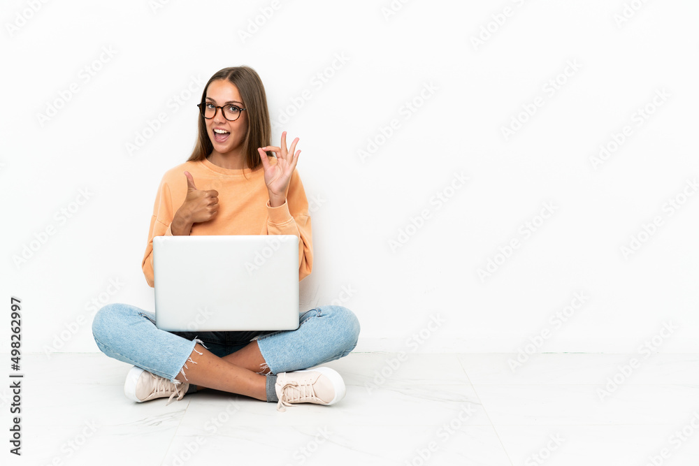 Young woman with a laptop sitting on the floor showing ok sign and thumb up gesture Young woman with a laptop sitting on the floor showing ok sign and thumb up gesture