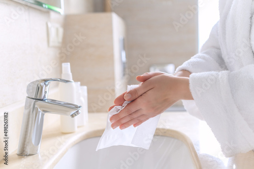 Fotografie Woman in a robe wiping hands with a paper napkin after washing hands in the bathroom