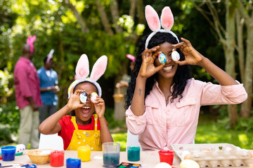Happy african american girl and mother playing with easter eggs while family in background