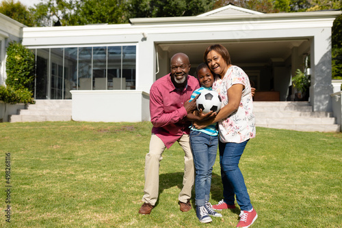 Portrait of happy african american grandparents with grandson holding soccer ball in front yard