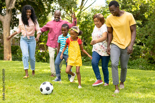 Happy african american multi-generational family playing soccer in backyard on weekend