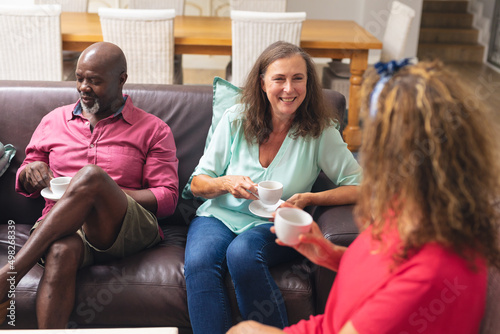 Smiling multiracial senior female and male friends talking while having coffee together at home