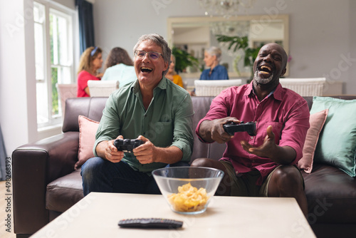 Happy multiracial senior male friends playing video game at home