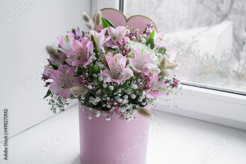 Delicate bouquet of pink lilies, white roses and gypsophila in a love word gift box on the window