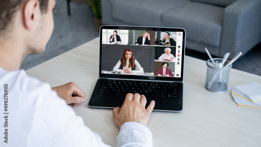 Web conference. Group video call. Distance communication. Male employee using laptop working from home with female business team on screen in digital office. Web conference. Group video call. Distance communication. Male employee using laptop working from home with female business team on screen in digital office.