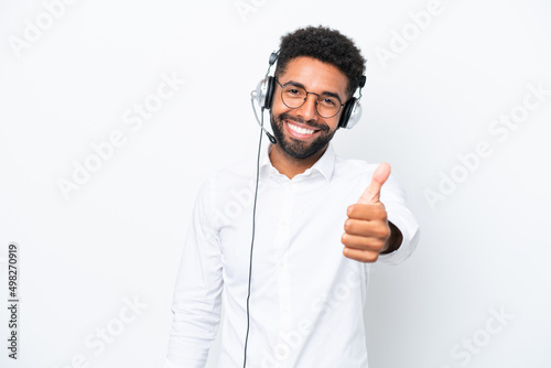 Telemarketer Brazilian man working with a headset isolated on white background with thumbs up because something good has happened © luismolinero