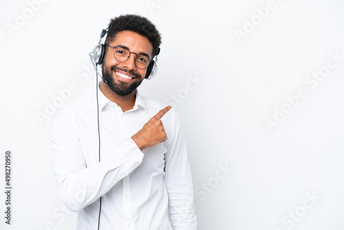 Telemarketer Brazilian man working with a headset isolated on white background pointing to the side to present a product