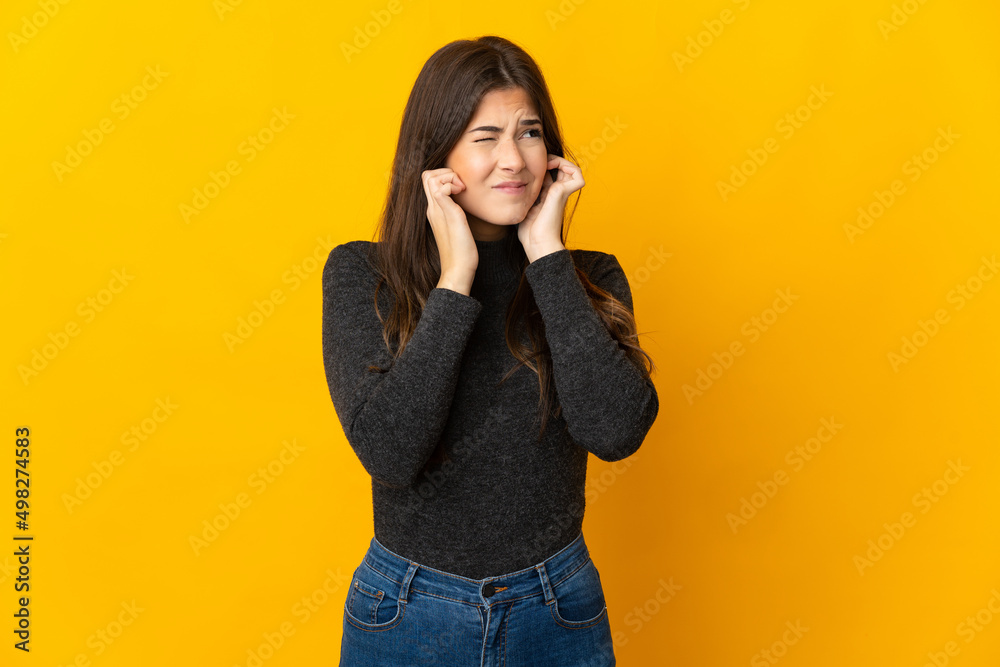 Teenager Brazilian girl isolated on yellow background frustrated and covering ears Teenager Brazilian girl isolated on yellow background frustrated and covering ears
