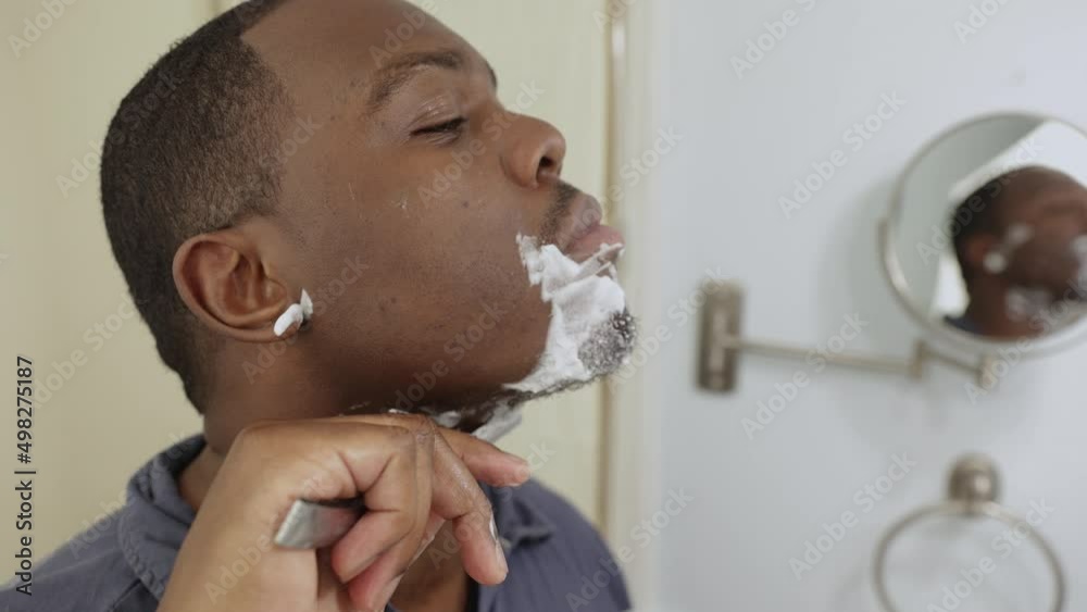 personal hygiene, African American or black man at home in bathroom using razor blade to shave beard as a barber would
