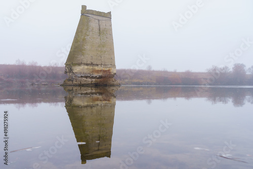 Concrete support of the blown up bridge on the river in damp foggy weather. Consequences of the war. Background photo