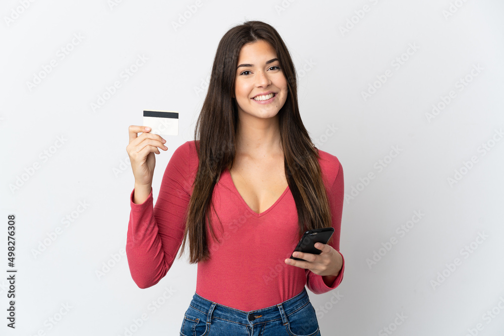Teenager Brazilian girl isolated on white background buying with the mobile with a credit card Teenager Brazilian girl isolated on white background buying with the mobile with a credit card