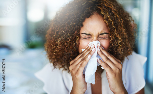 I think Im going to the doctor later. Shot of a frustrated businesswoman using a tissue to sneeze in while being seated in the office. © Delmaine Donson/peopleimages.com