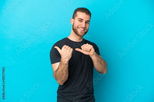 Young handsome caucasian man isolated on blue background pointing to the side to present a product