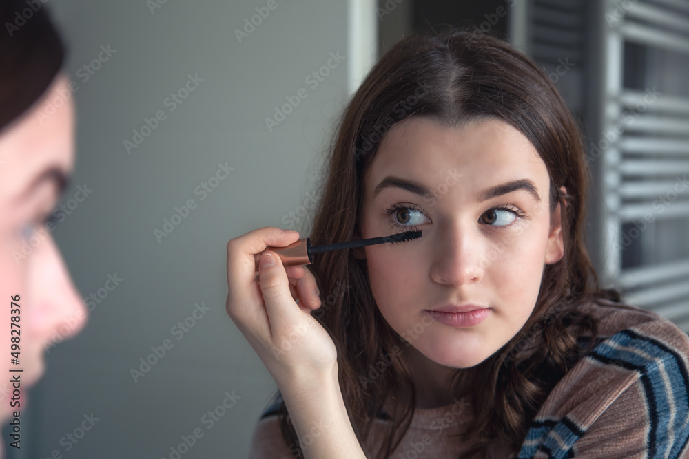 A young woman paints her eyelashes with mascara in front of a mirror. A young woman paints her eyelashes with mascara in front of a mirror.