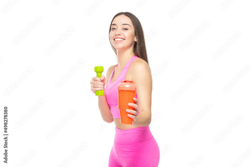 A beautiful, athletic, slim, smiling and cheerful woman in a pink tracksuit holds a dumbbell and a shaker with water. Lifestyle concept with sports and gym. Isolated on white background. A beautiful, athletic, slim, smiling and cheerful woman in a pink tracksuit holds a dumbbell and a shaker with water. Lifestyle concept with sports and gym. Isolated on white background.