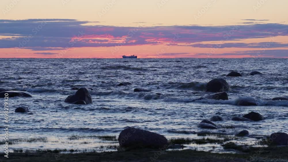 sunset on the sea. The shore is strewn with huge stones on which the waves break. The sun left a red trail in the sky. the silhouette of a tanker is visible on the horizon sunset on the sea. The shore is strewn with huge stones on which the waves break. The sun left a red trail in the sky. the silhouette of a tanker is visible on the horizon