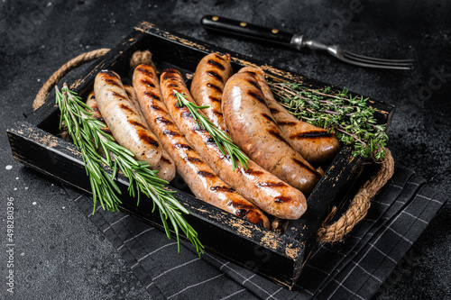 Fried on a grill skillet mix sausages in a wooden tray with herbs. Black background. Top view