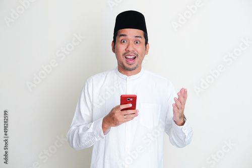 Moslem Asian man showing amazed expression while holding mobile phone photo