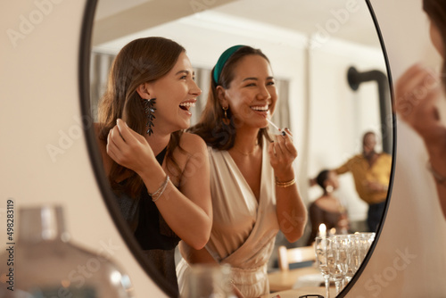 We always have a joke prepared. Shot of two young friends standing together and using a mirror to touch up their makeup at a dinner party.