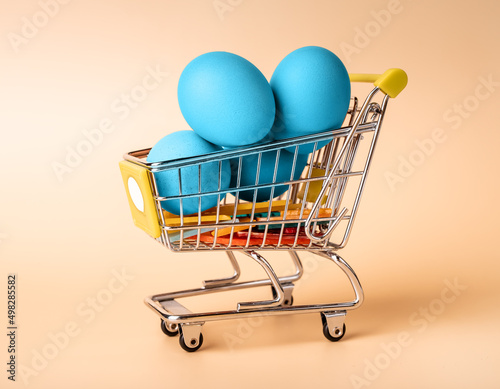 Blue painted Easter eggs in supermarket trolley. Symbol of religious holiday concept on beige background. High quality photo
