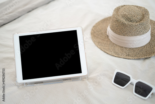 iPad white blank glasses and a brown straw hat on the bed holiday concept