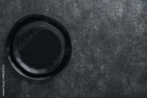 Ceramic empty black plate on old black ceramic cement concrete table background. Cooking stone backdrop. Top view with copy space. Flat lay