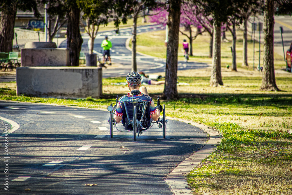 Naklejka premium Man on recumbent bicycle on paved trail in park in springtime - selective focus