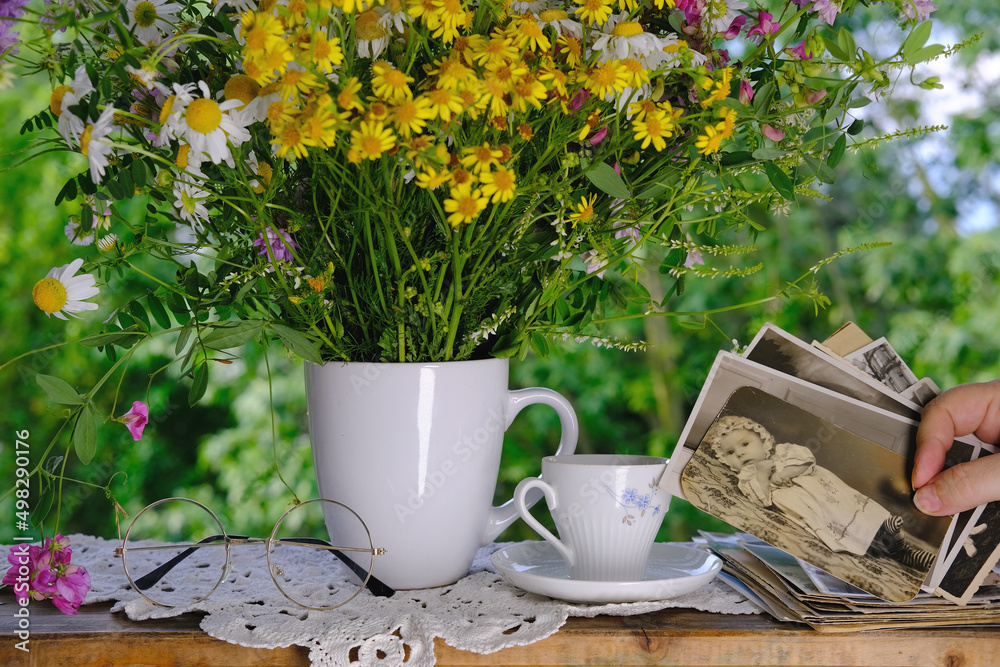 female hands going through old photos of 40s, 50s, bouquet of wildflowers, handmade lacy, cup of tea on table in garden, concept of genealogy, memory of ancestors, family tree, family archive female hands going through old photos of 40s, 50s, bouquet of wildflowers, handmade lacy, cup of tea on table in garden, concept of genealogy, memory of ancestors, family tree, family archive