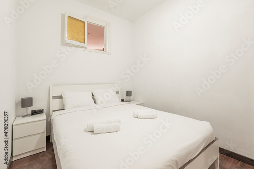 Bedroom with king size bed with white wooden headboard with matching side tables and rolled up white towels