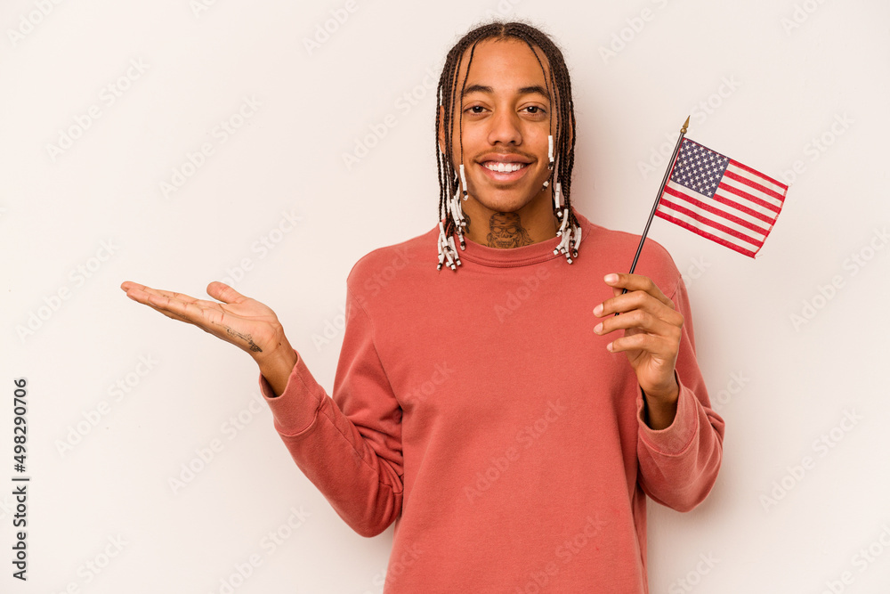 Young African American man holding a American flag isolated on white background showing a copy space on a palm and holding another hand on waist. Young African American man holding a American flag isolated on white background showing a copy space on a palm and holding another hand on waist.