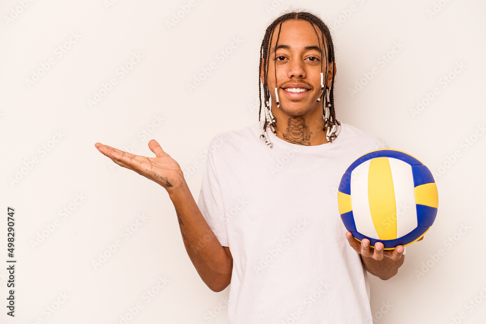 Young African American man playing volleyball isolated on white background showing a copy space on a palm and holding another hand on waist.