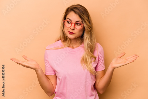 Young caucasian woman isolated on beige background confused and doubtful shrugging shoulders to hold a copy space.